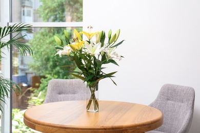 Vase with bouquet of beautiful lilies on wooden table indoors