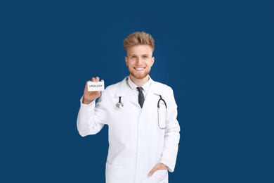 Male doctor holding card with word UROLOGY on blue background