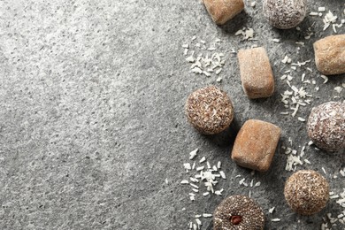 Photo of Different delicious vegan candy balls and desiccated coconut on grey table, flat lay. Space for text