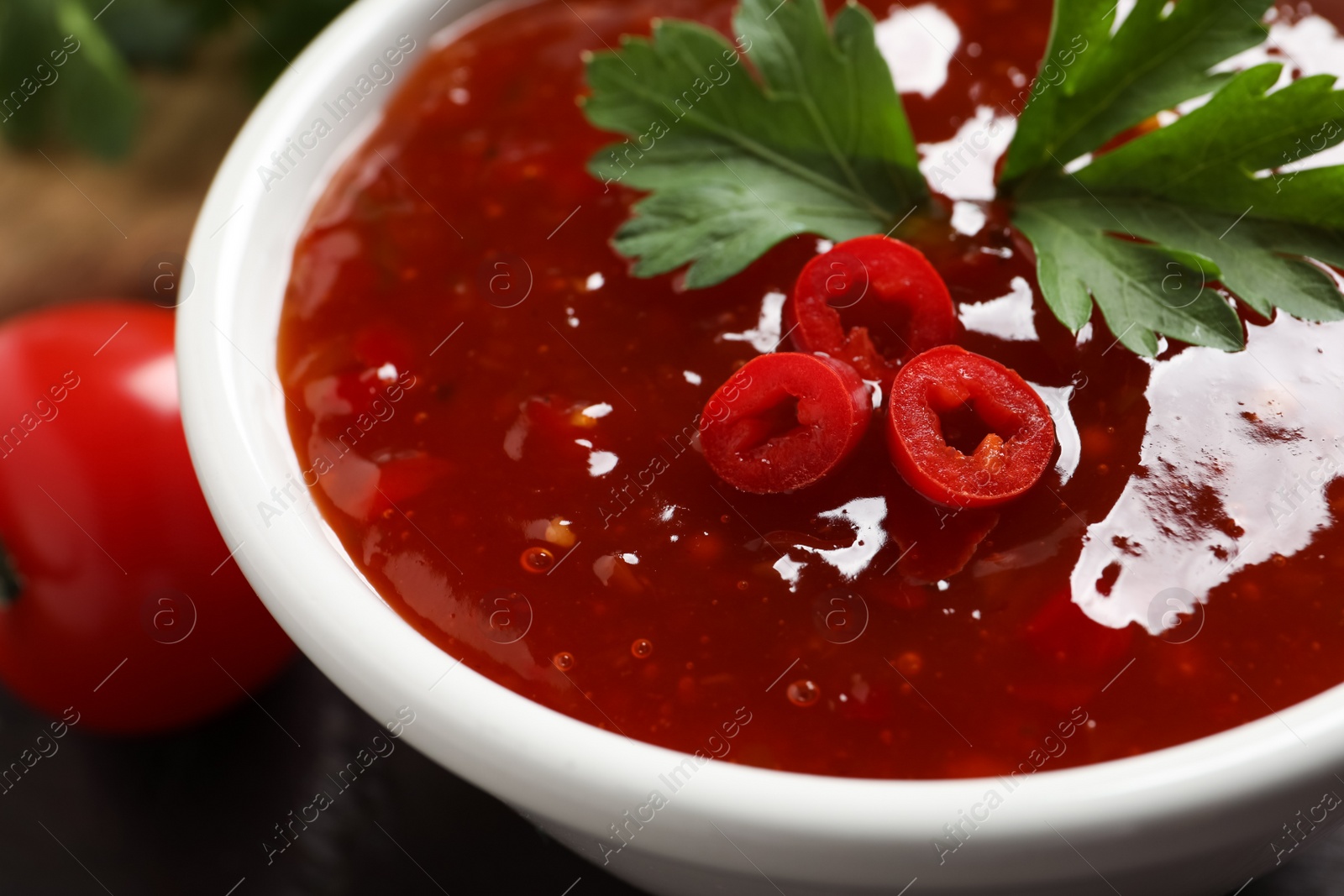 Photo of Spicy chili sauce with parsley on table, closeup