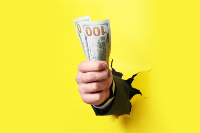 Photo of Businessman breaking through yellow paper with money in fist, closeup