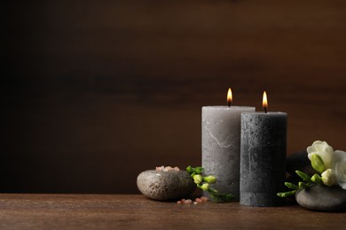 Photo of Beautiful composition with burning candles, spa stones and flowers on wooden table. Space for text