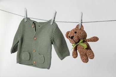 Photo of Baby shirt and toy bear drying on laundry line against light background