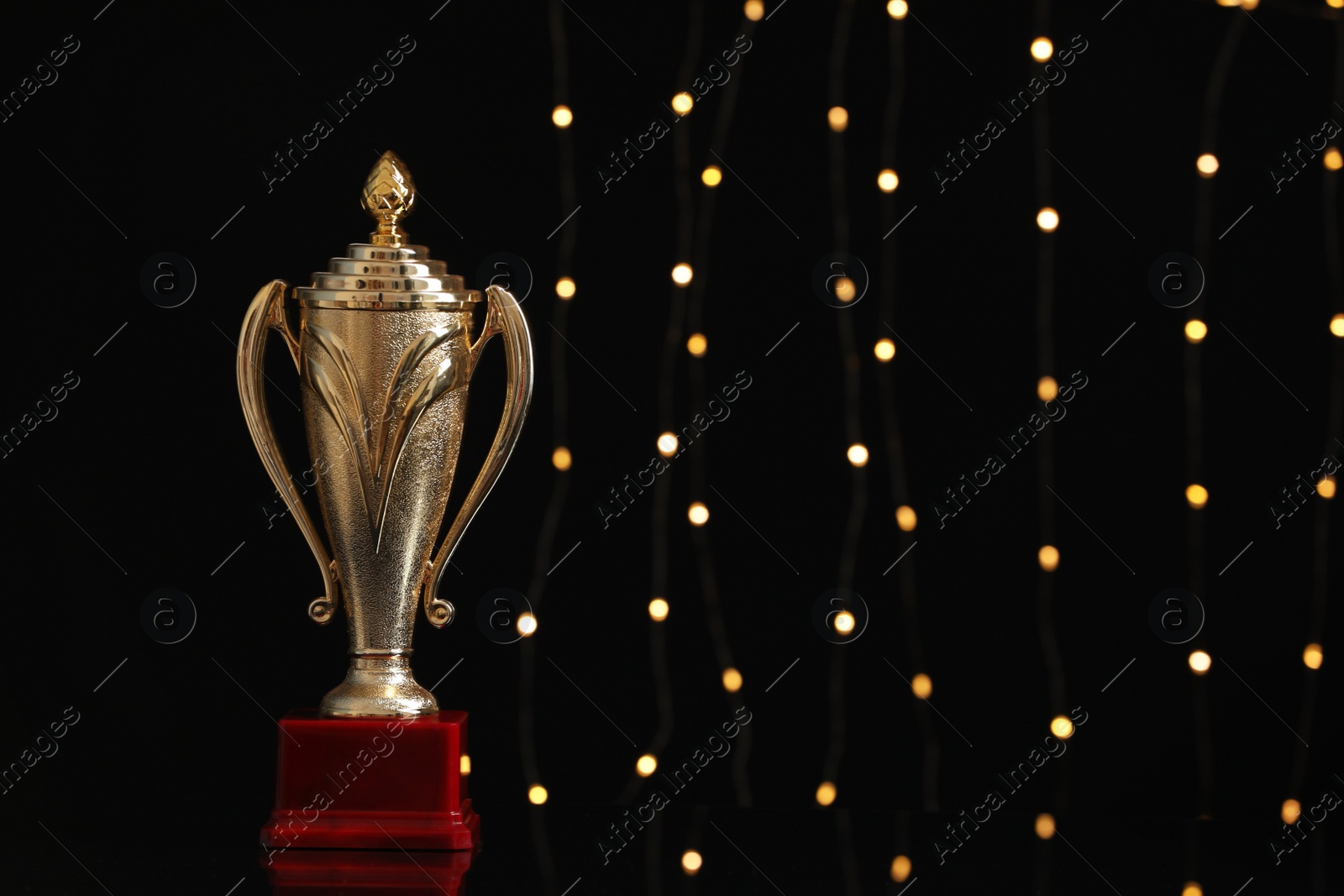 Photo of Golden trophy cup against blurred festive lights, space for text