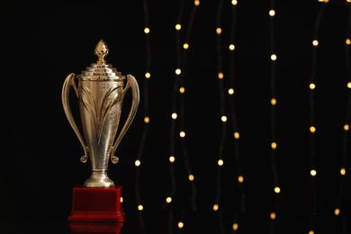 Photo of Golden trophy cup against blurred festive lights, space for text