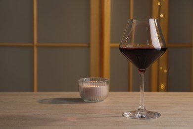 Glass of red wine and candle on wooden table indoors, space for text