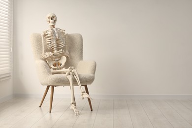 Waiting concept. Human skeleton sitting in armchair indoors, space for text