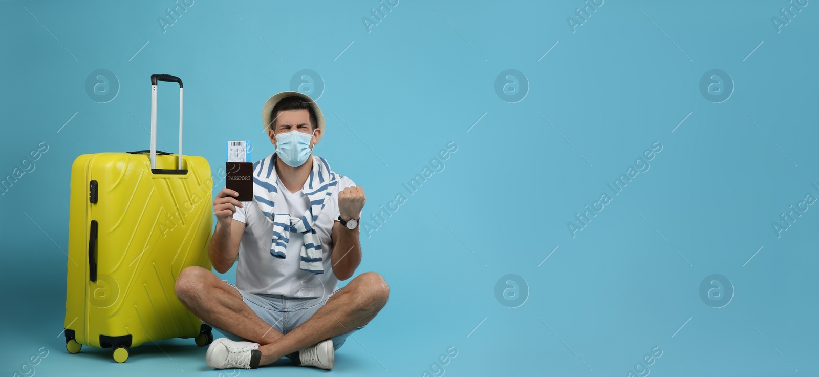 Photo of Male tourist in protective mask holding passport with ticket near suitcase on turquoise background