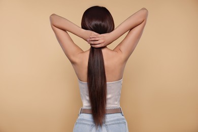 Beautiful woman with strong healthy hair on beige background, back view