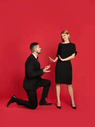 Photo of Young woman rejecting engagement ring from boyfriend on red background