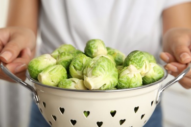 Woman holding colander with Brussels sprouts on blurred background, closeup