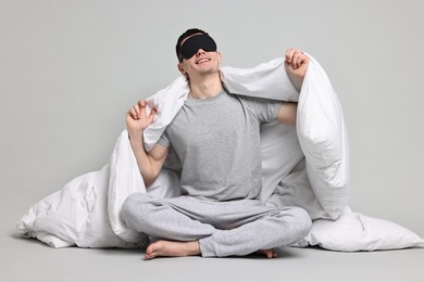 Photo of Happy man in pyjama and sleep mask wrapped in blanket on grey background