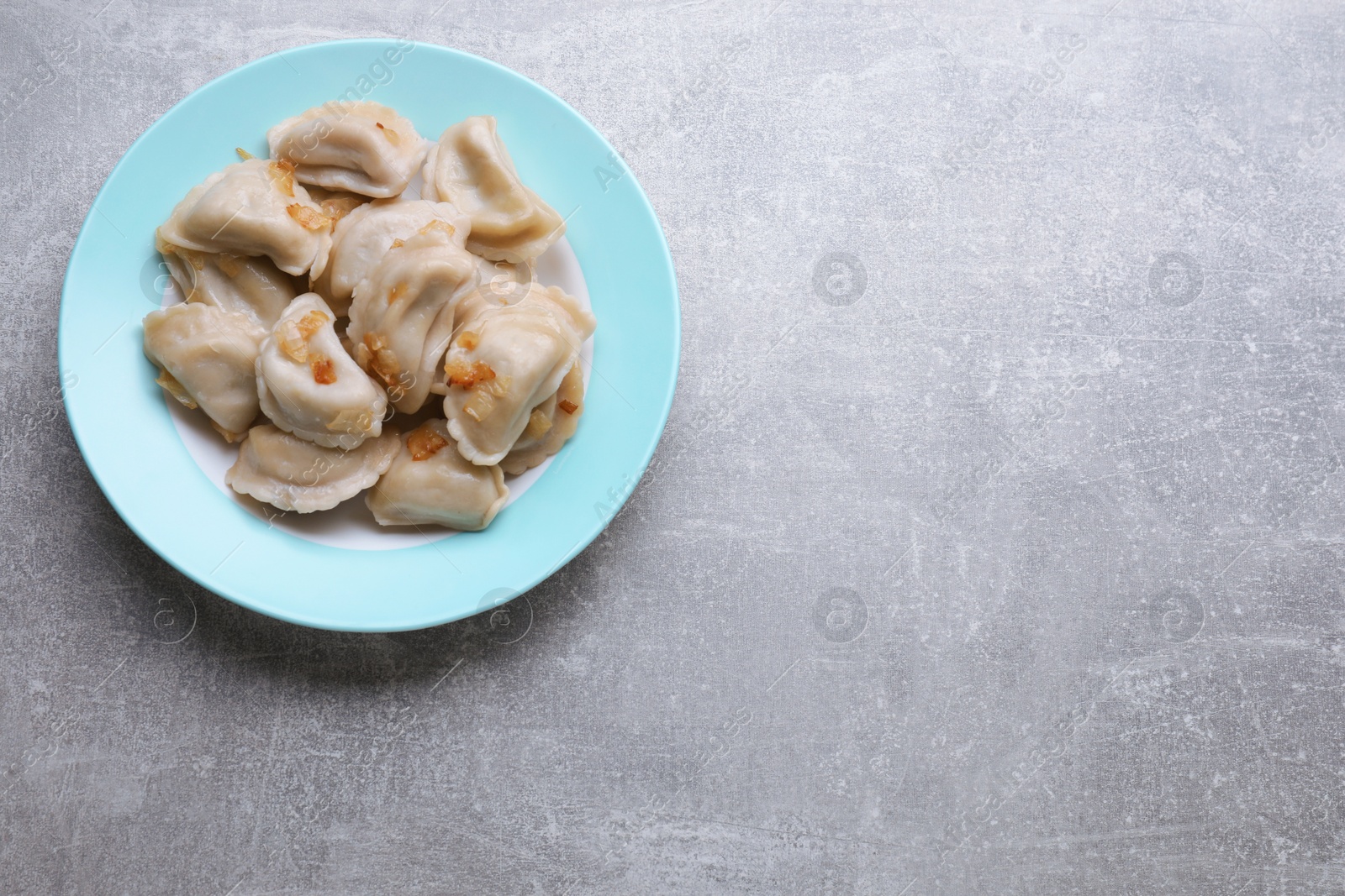 Photo of Delicious dumplings (varenyky) with potatoes and onion on grey table, top view. Space for text