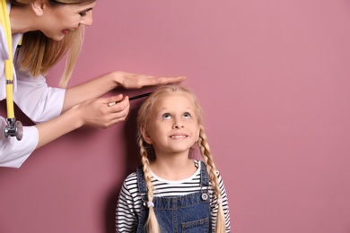 Doctor measuring little girl's height on color background