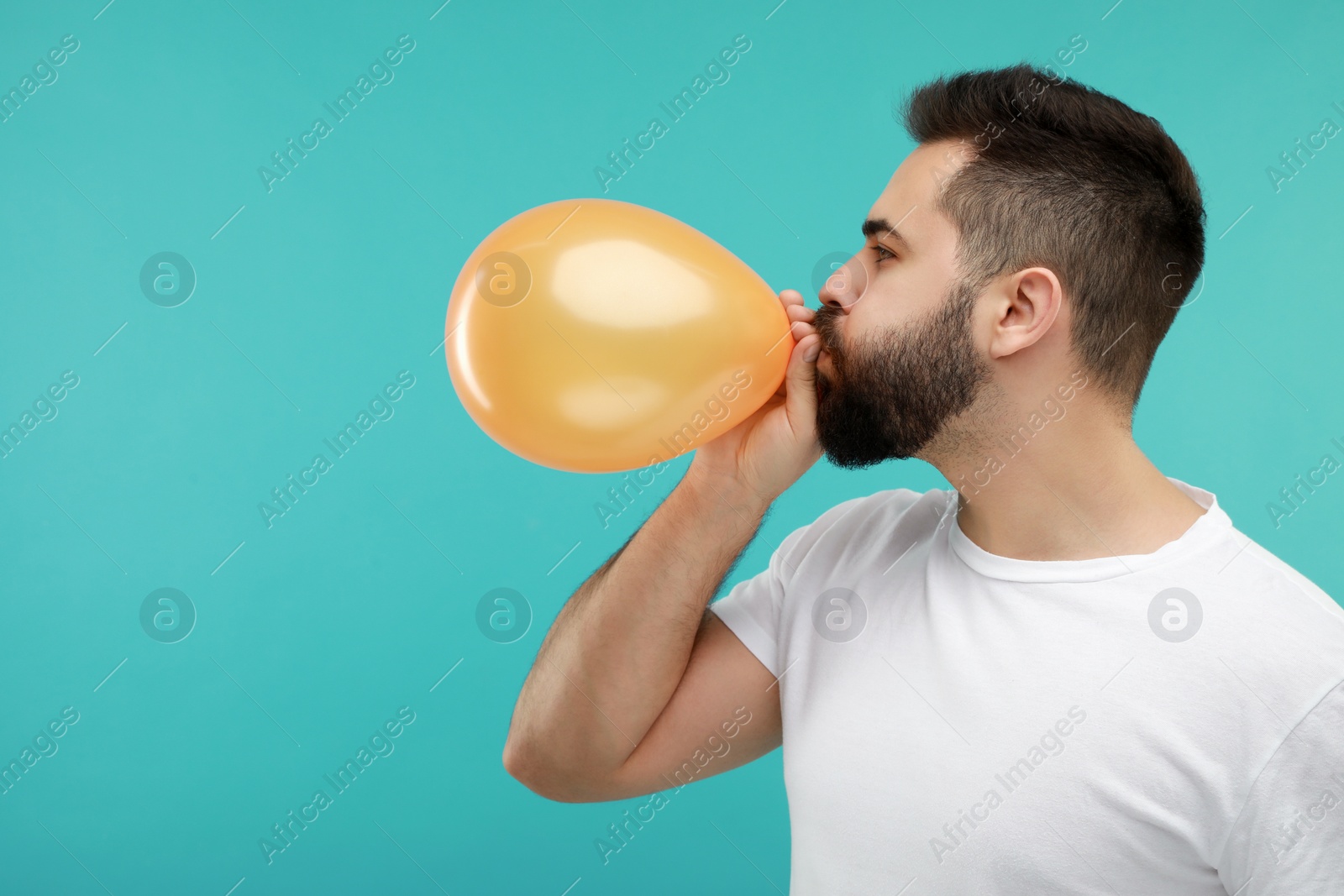 Photo of Man inflating bright balloon on turquoise background, space for text