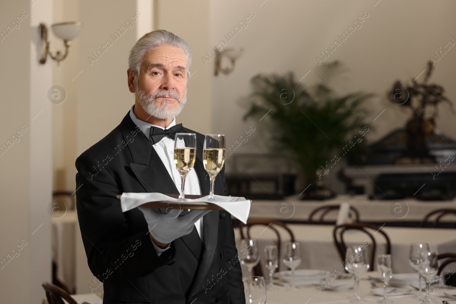 Photo of Senior butler holding tray with glasses of sparkling wine in restaurant. Space for text