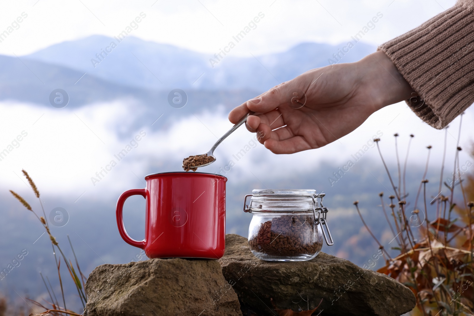 Photo of Woman pouring instant coffee into mug in mountains, closeup