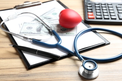 Stethoscope, clipboard and red heart on wooden surface. Health insurance concept