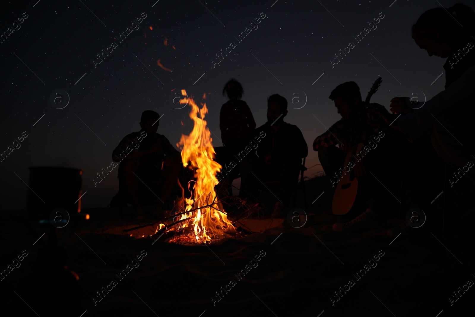 Photo of Group of friends gathering around bonfire at night. Camping season