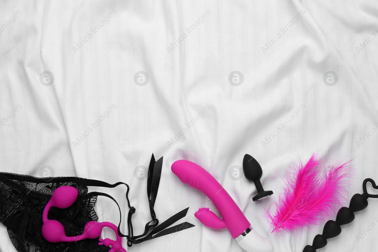 Photo of Sex toys and accessories on white fabric, flat lay. Space for text