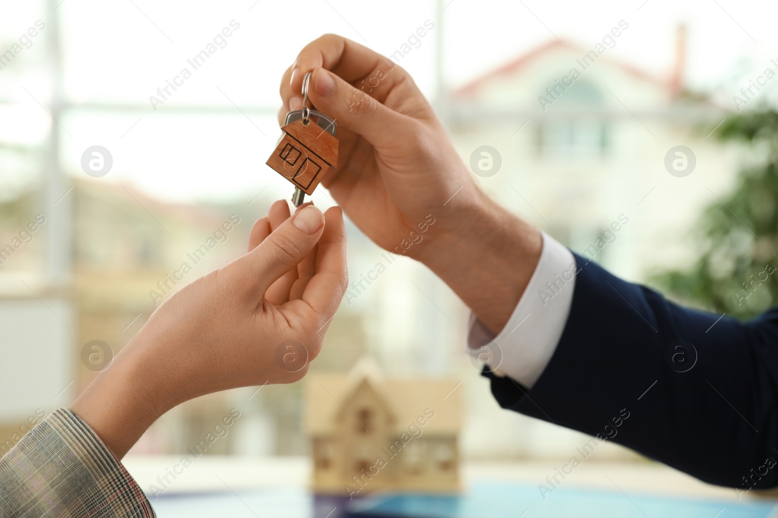 Photo of Real estate agent giving key with trinket to client in office, closeup