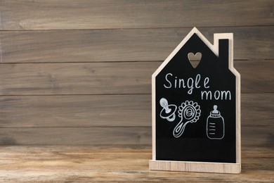Photo of Chalkboard with words Single Mom and baby accessories on wooden table. Space for text