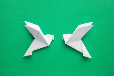 Beautiful white origami birds on green background, flat lay