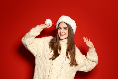 Photo of Young woman in Christmas sweater and Santa hat on red background