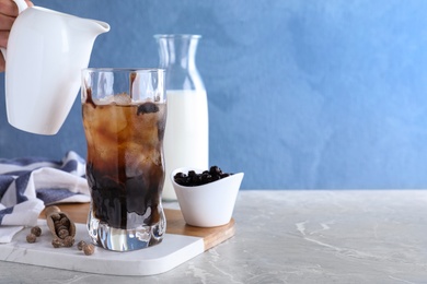 Person preparing bubble milk tea with tapioca balls at grey marble table against blue background. Space for text