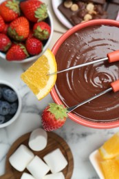 Photo of Fondue pot with melted chocolate, marshmallows, fresh orange, different berries and forks on white marble table, flat lay