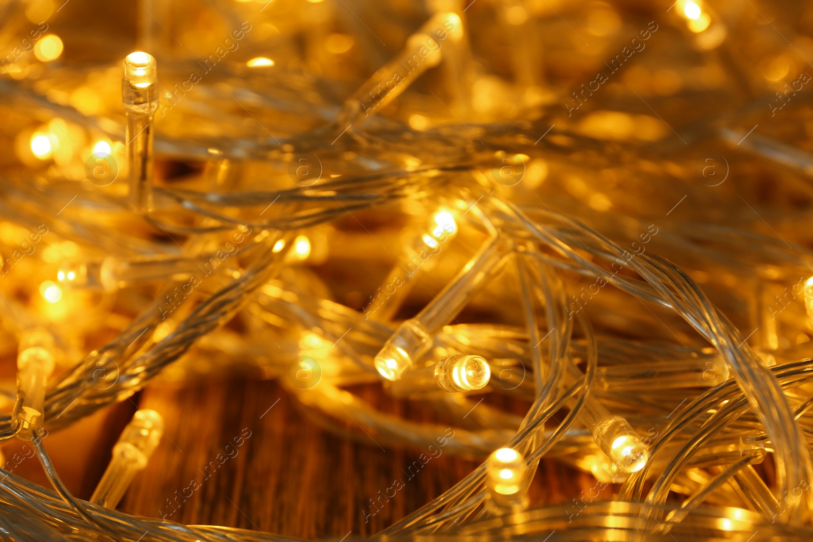 Photo of Glowing Christmas lights on wooden table, closeup view