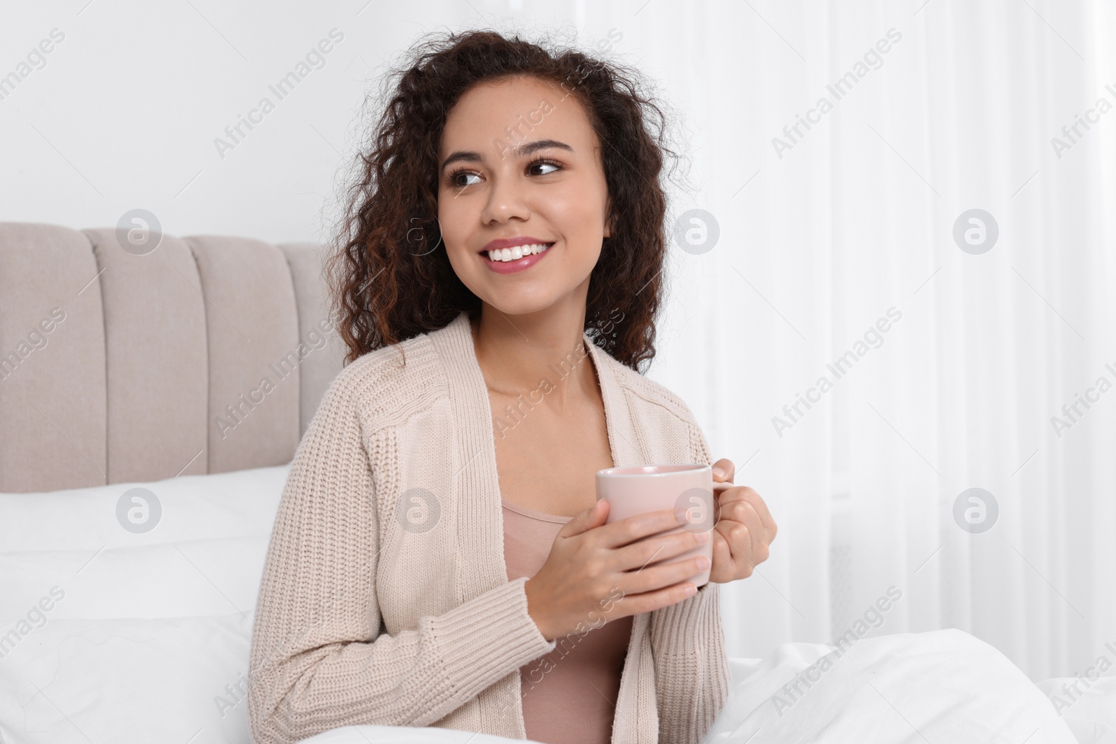 Photo of Happy African American woman with cup of drink in bed at home