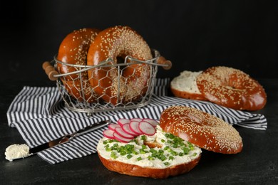 Photo of Delicious bagel with cream cheese, radish and green onion on black table