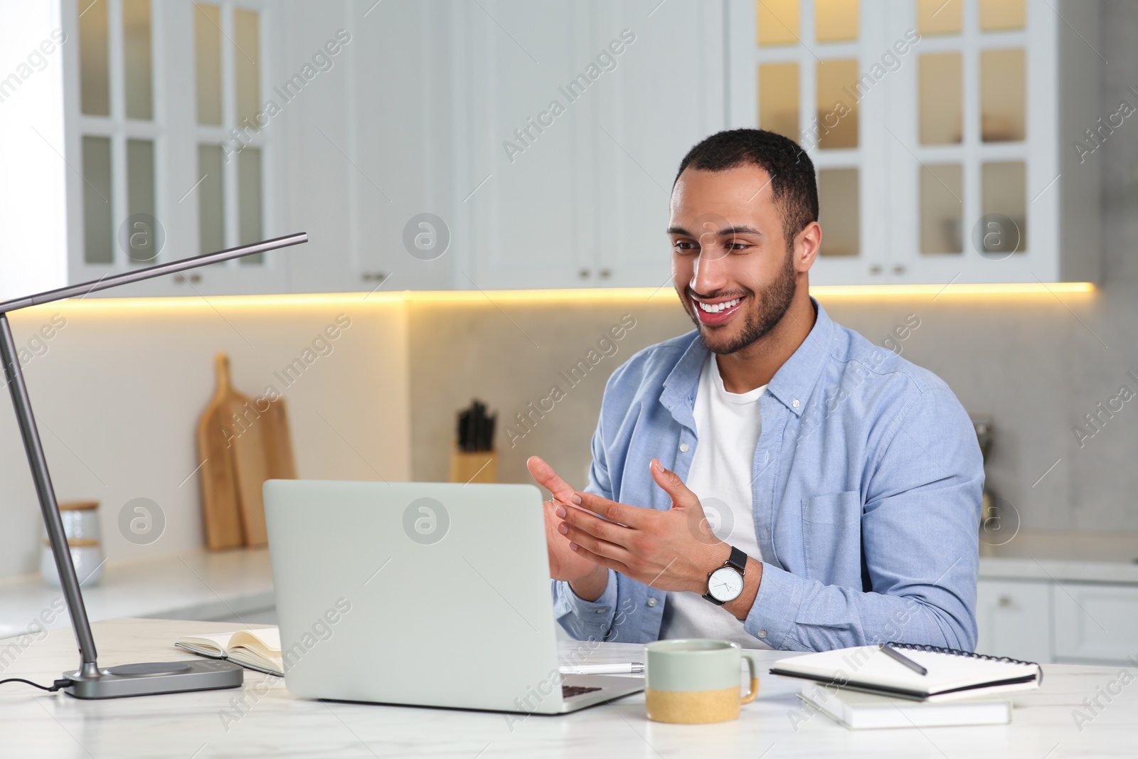 Photo of Young man having online video chat at desk in kitchen. Home office