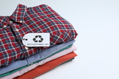 Photo of Stack of clothes with recycling label on white background, space for text