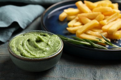Plate with delicious french fries, avocado dip and rosemary served on grey wooden table, closeup
