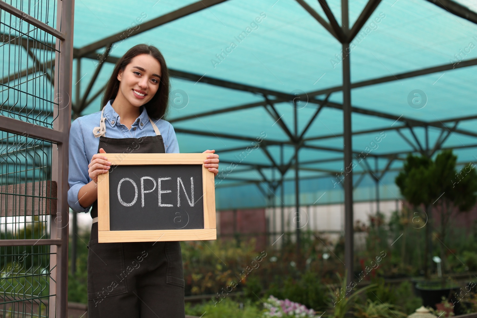 Photo of Female business owner holding OPEN sign in greenhouse. Space for text