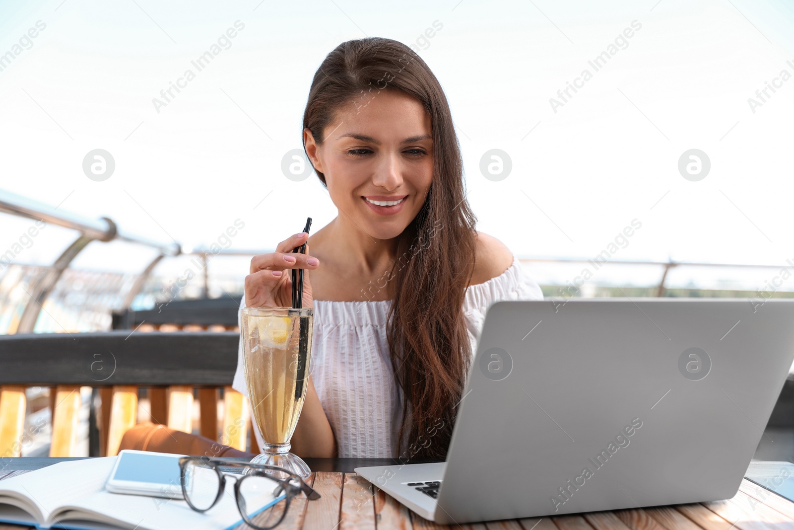 Photo of Beautiful woman with refreshing drink and laptop at outdoor cafe