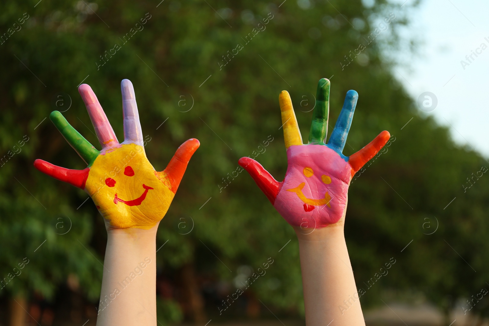 Photo of Kid with smiling face drawn on palms in green park, closeup