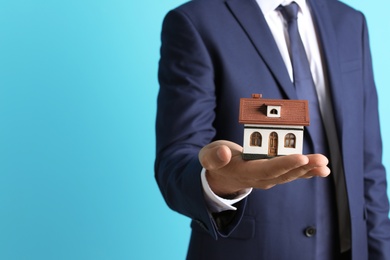 Real estate agent holding house model on color background, closeup