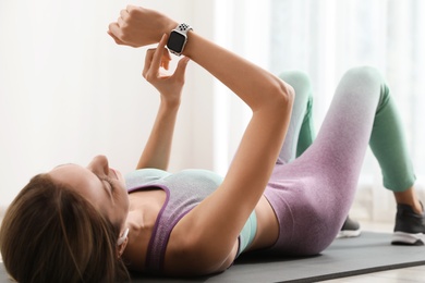 Photo of Young woman using smart watch during training indoors