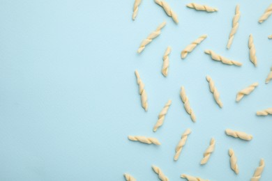 Photo of Uncooked trofie pasta on light blue background, flat lay. Space for text