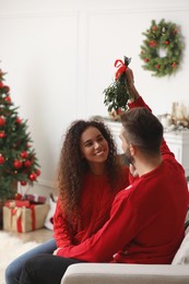 Photo of Lovely couple sitting under mistletoe bunch in room decorated for Christmas