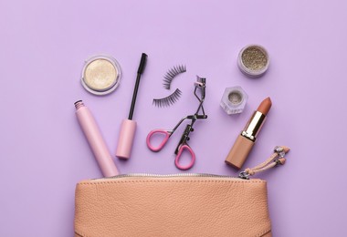 Eyelash curler, cosmetic bag and makeup products on violet background, flat lay