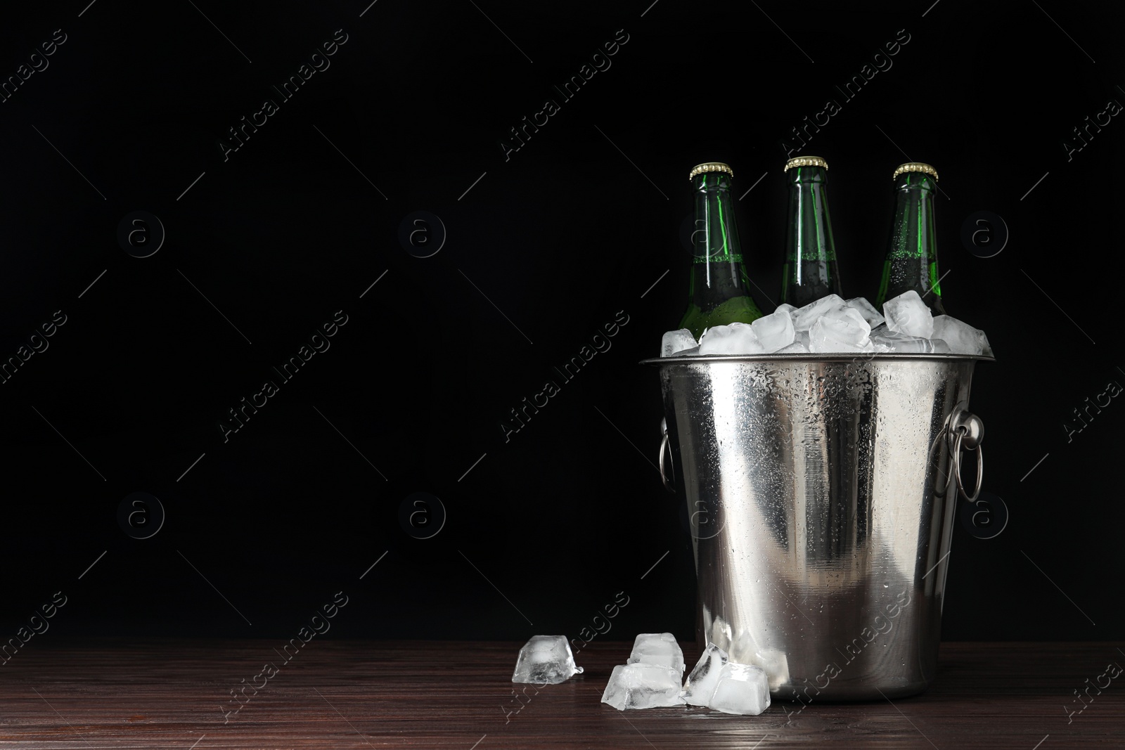 Photo of Metal bucket with bottles of beer and ice cubes on wooden table. Space for text