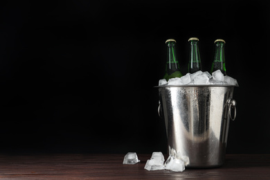 Metal bucket with bottles of beer and ice cubes on wooden table. Space for text