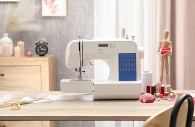 Photo of White sewing machine, cloth, craft accessories and mannequin on wooden table indoors