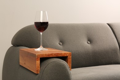 Photo of Glass of red wine on sofa with wooden armrest table in room, space for text. Interior element