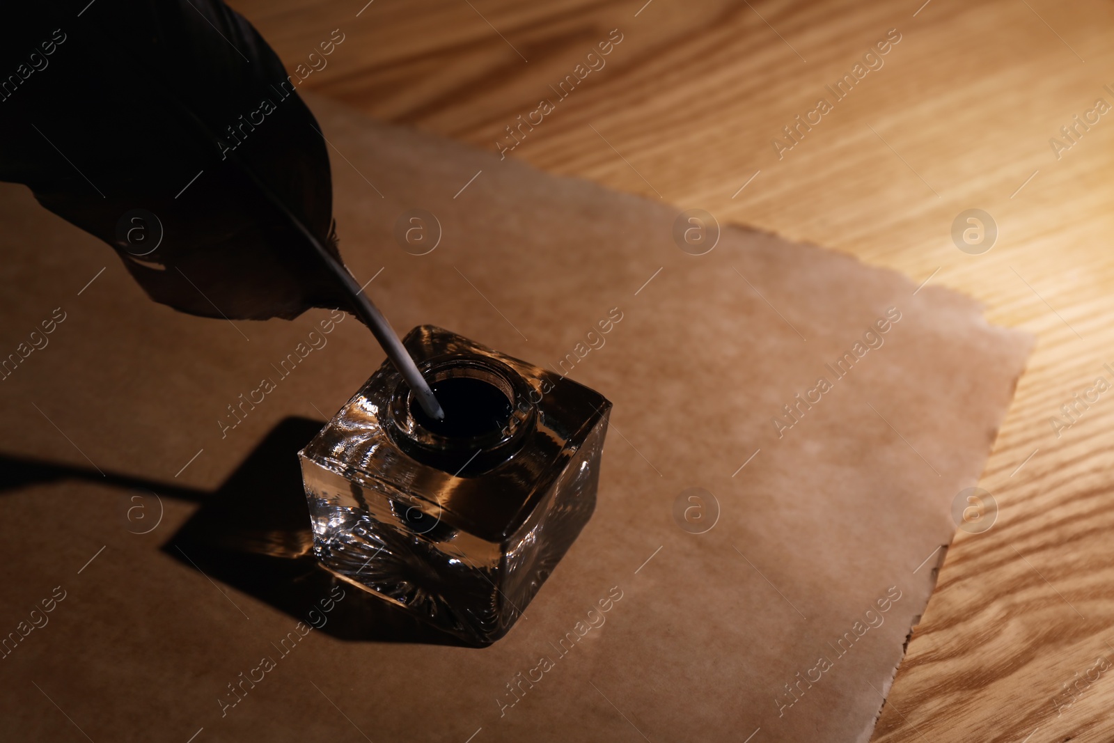 Photo of Feather pen, inkwell and blank parchment on wooden table. Space for text