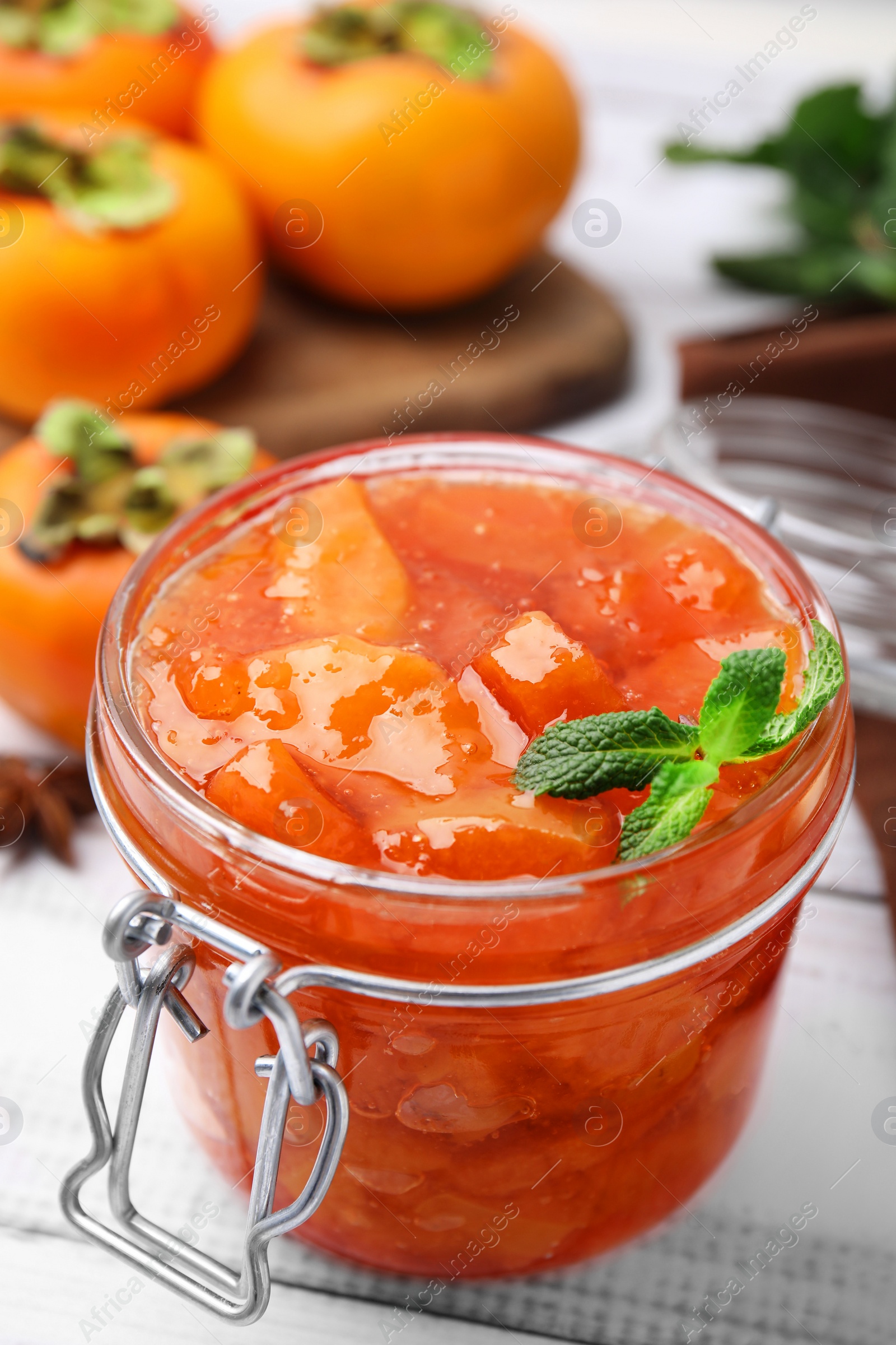 Photo of Jar of tasty persimmon jam and mint on white wooden table